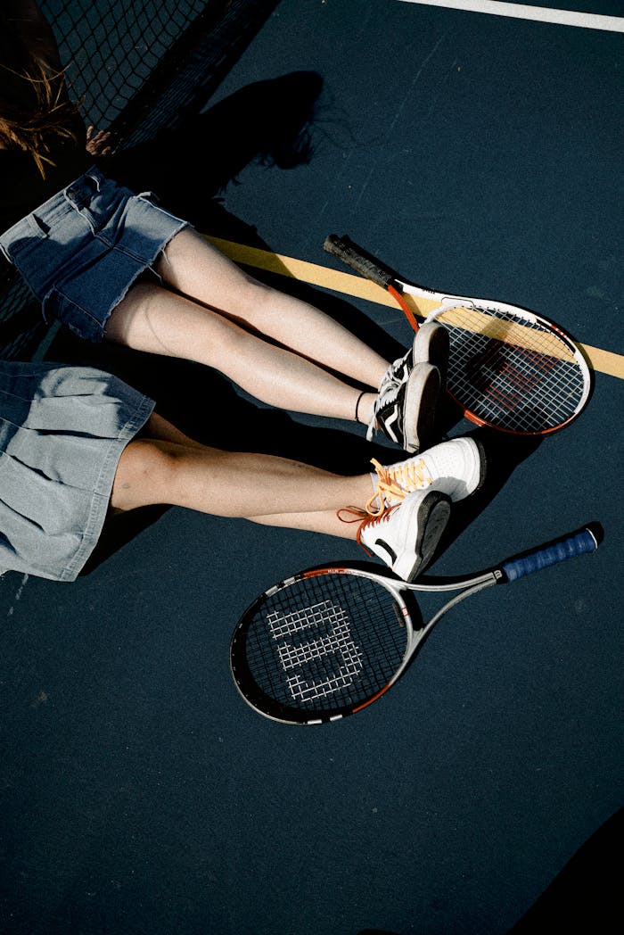 Two women resting on a tennis court with rackets, enjoying leisure outdoors.
