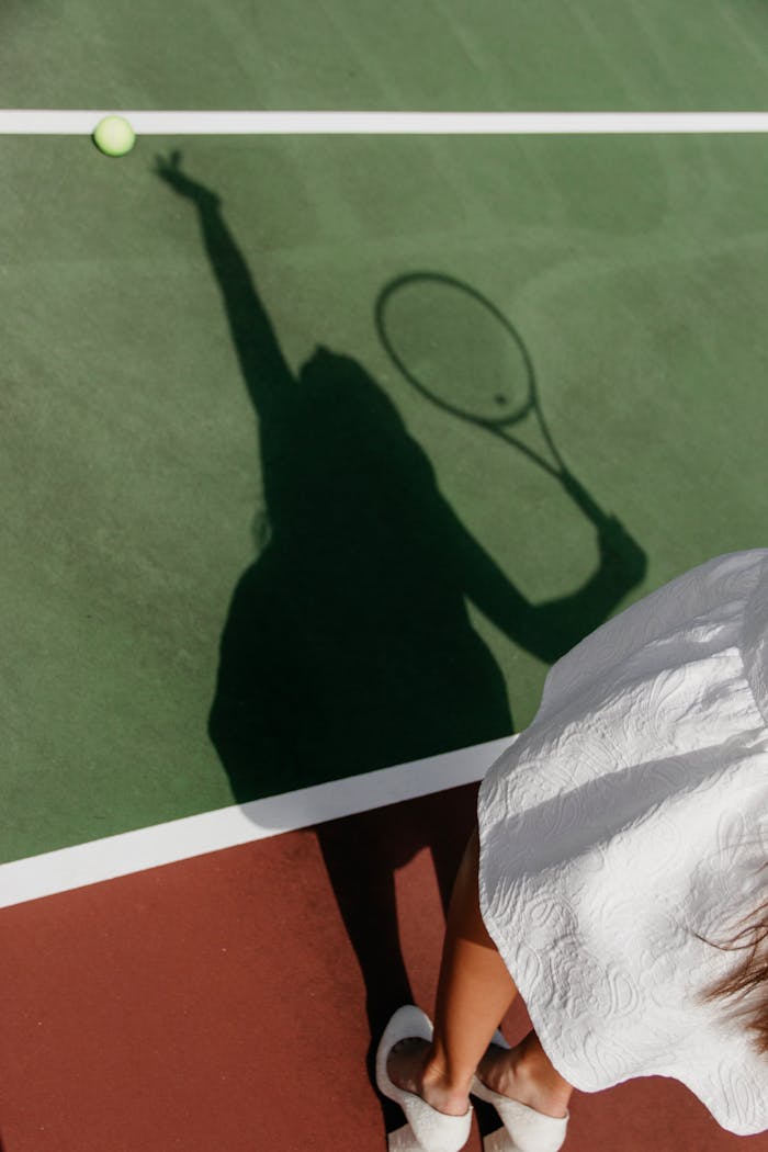 Shadow of a tennis player with racket on a green court, ready to serve.