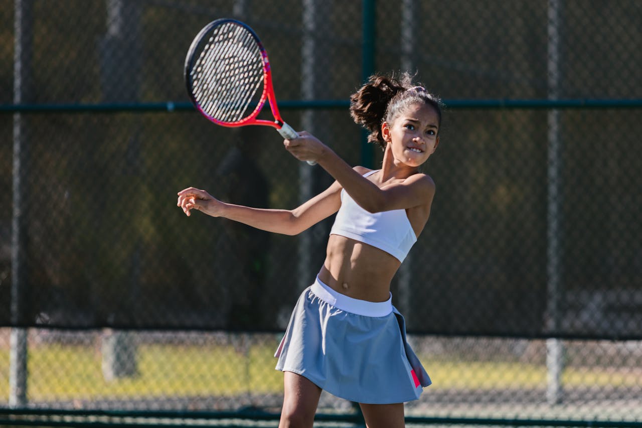 A young girl energetically hitting a tennis ball on an outdoor court, showcasing athleticism and fun.